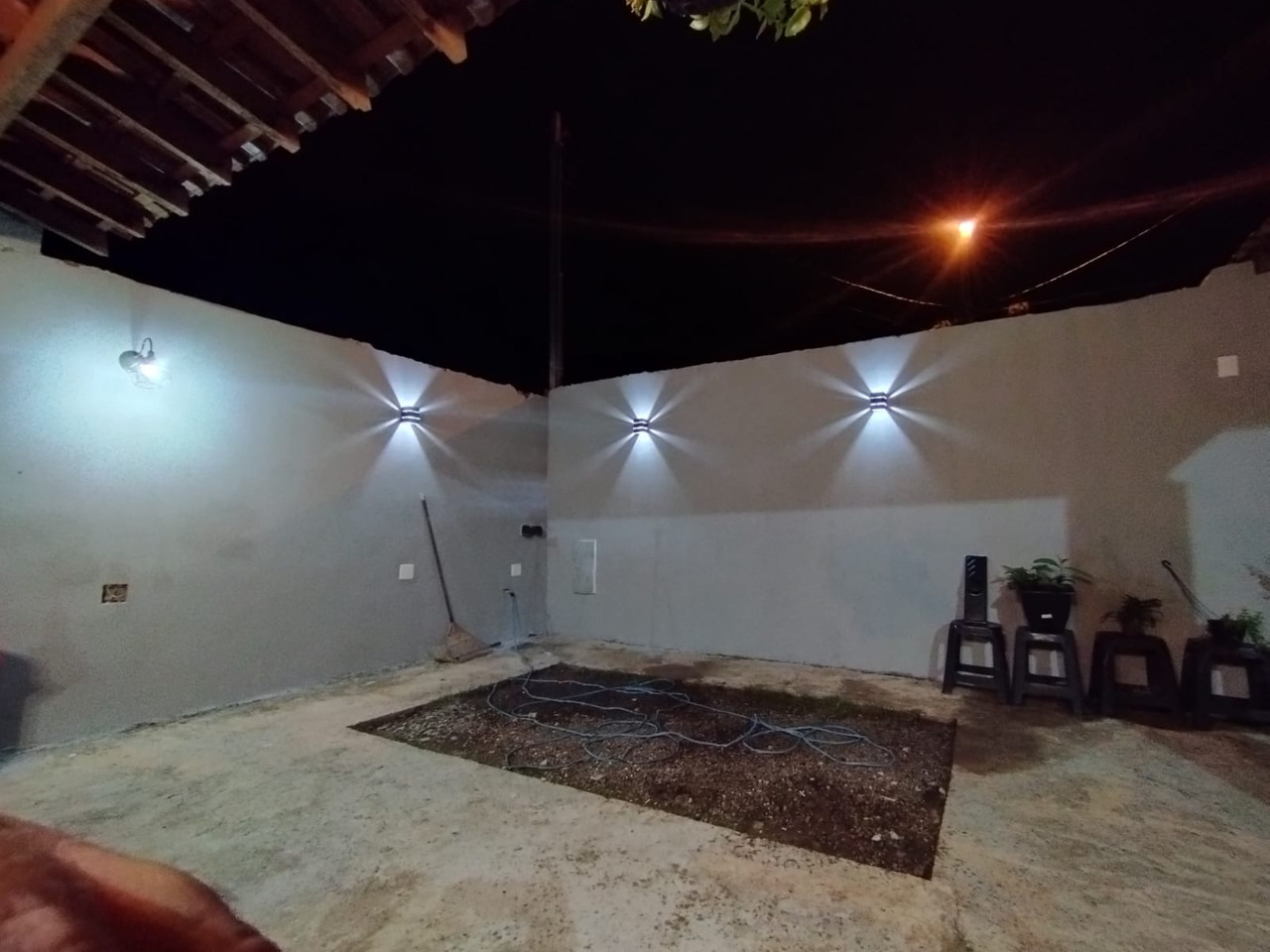 Parede externa a noite, pintada com a cor elefante e com iluminação pontual.