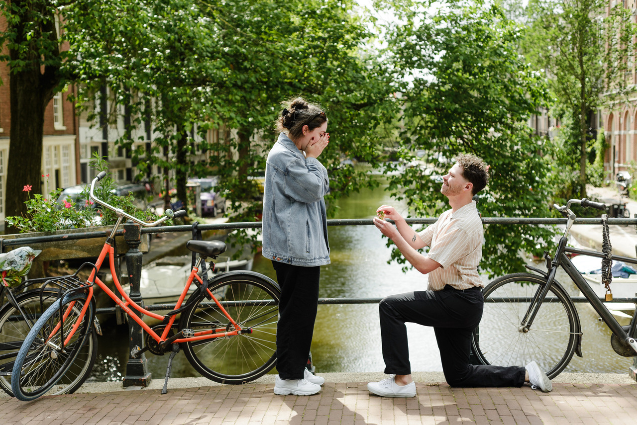 Woman covering her face with emotion as her partner proposes on a quiet Amsterdam canal bridge.
