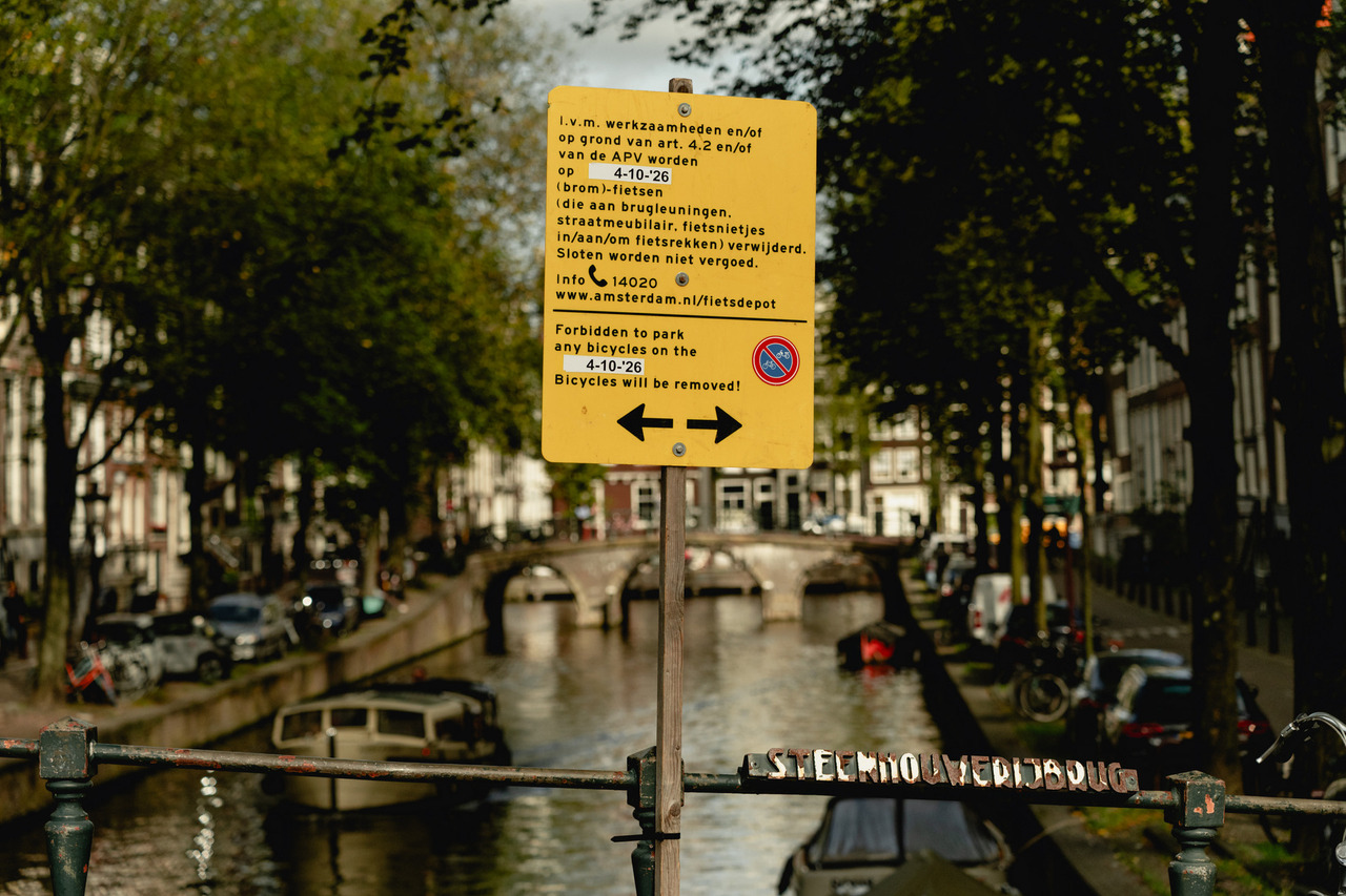 Yellow notice beside an Amsterdam bridge announcing bicycle removal on 4 October 2026.