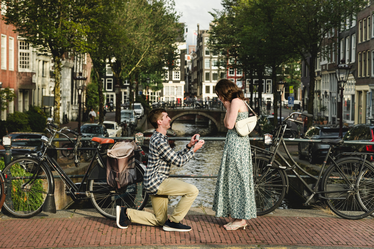 Man proposing to his partner on a canal bridge in Amsterdam during a sunny evening, surrounded by bicycles.