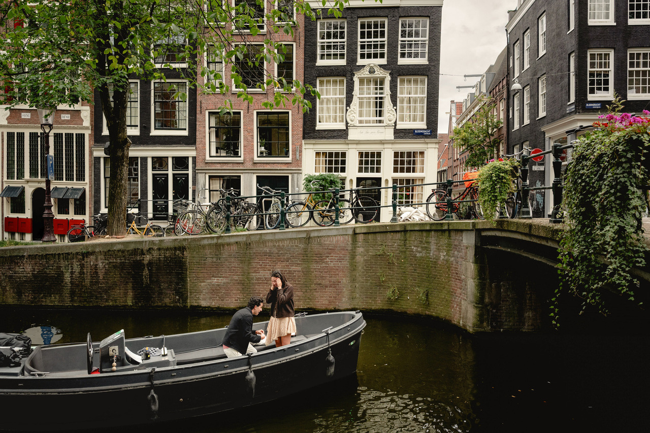 Man proposing to his partner on an open canal boat beneath a bridge in Amsterdam.
