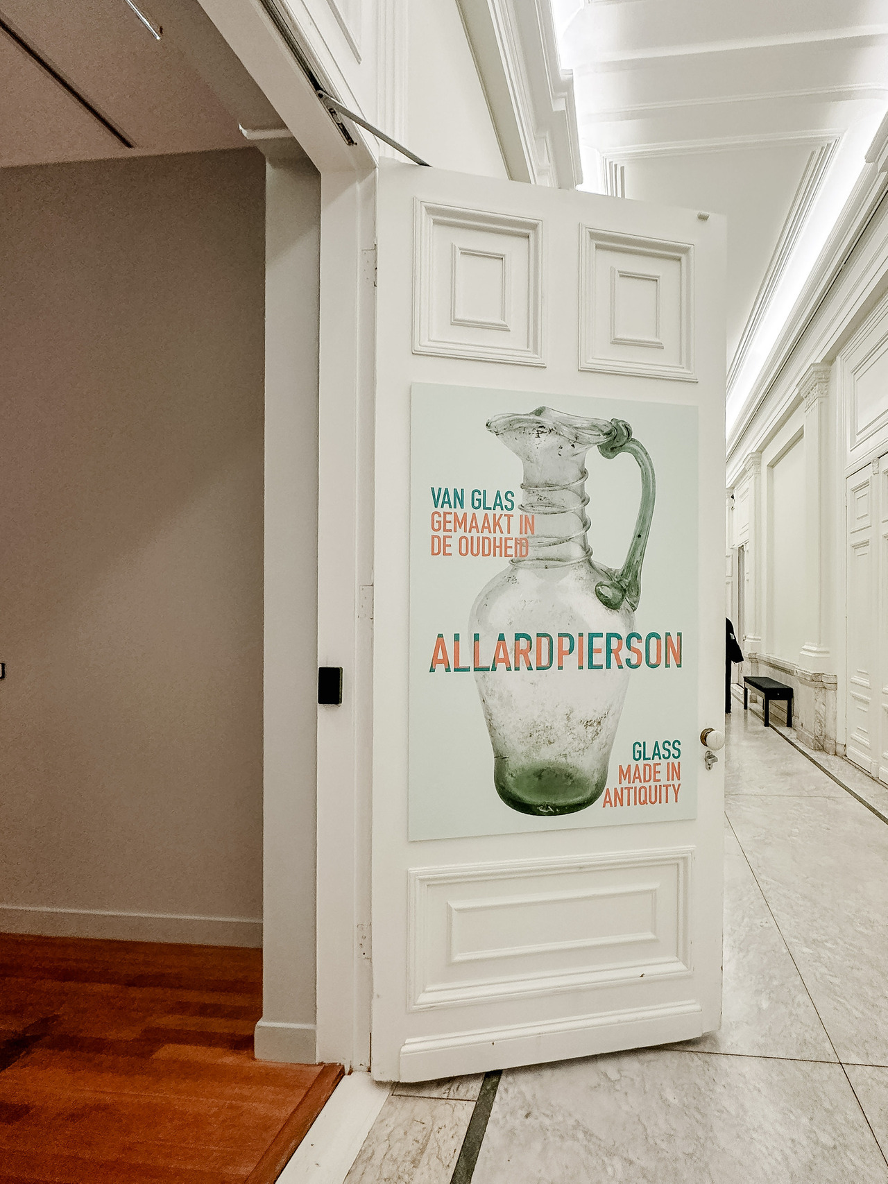 Entrance to the Glass, Made in Antiquity exhibition at the Allard Pierson Museum in Amsterdam, with a poster featuring an ancient glass jug.