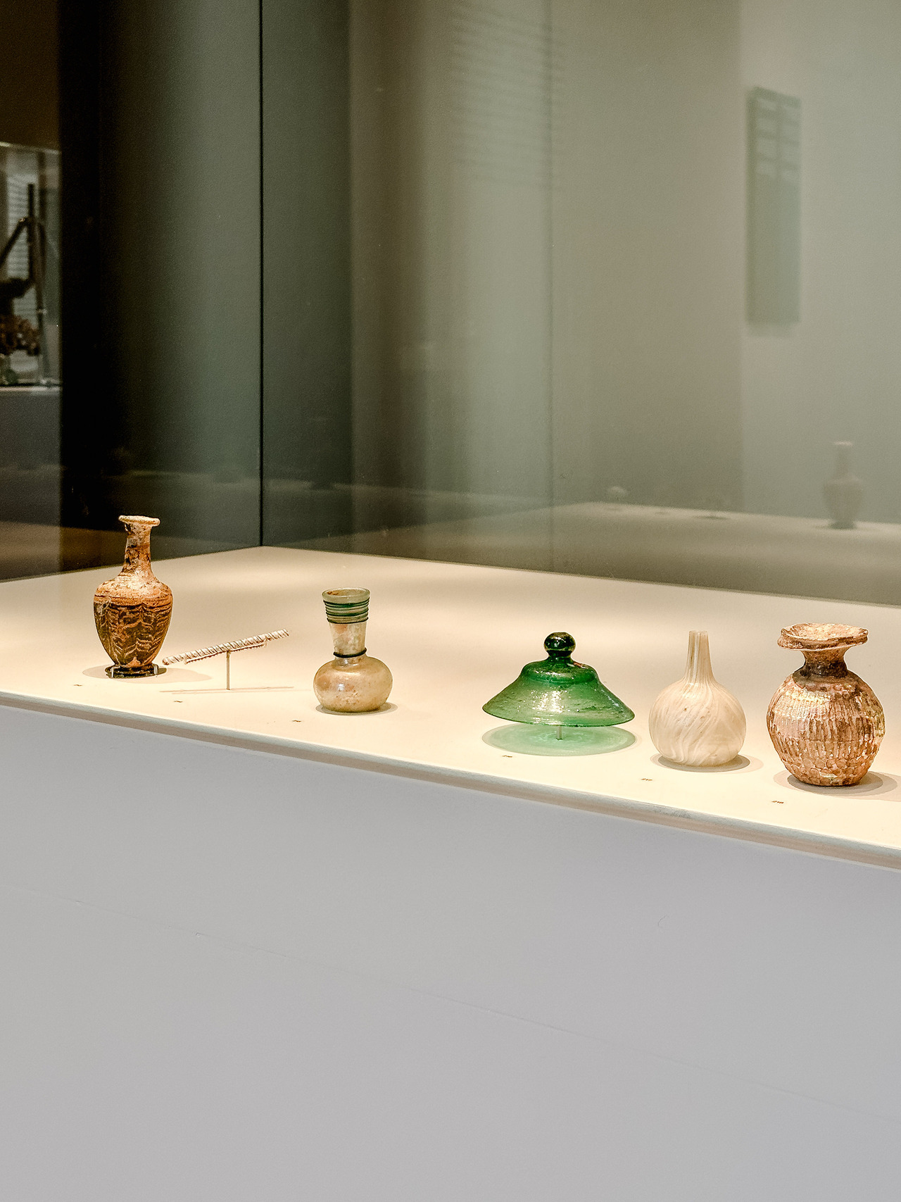 Ancient glass bottles, small vessels and a green glass lid arranged in a display case at the Allard Pierson Museum.