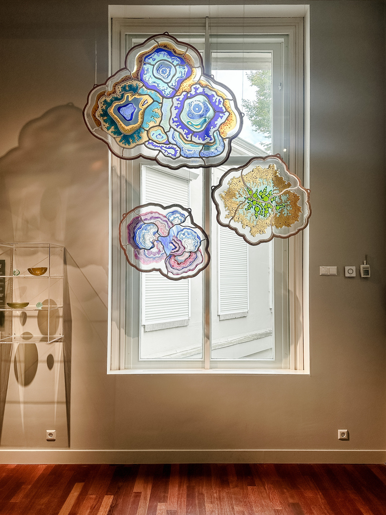 Three colourful, irregularly shaped glass artworks hanging in front of a tall window at the Allard Pierson Museum.