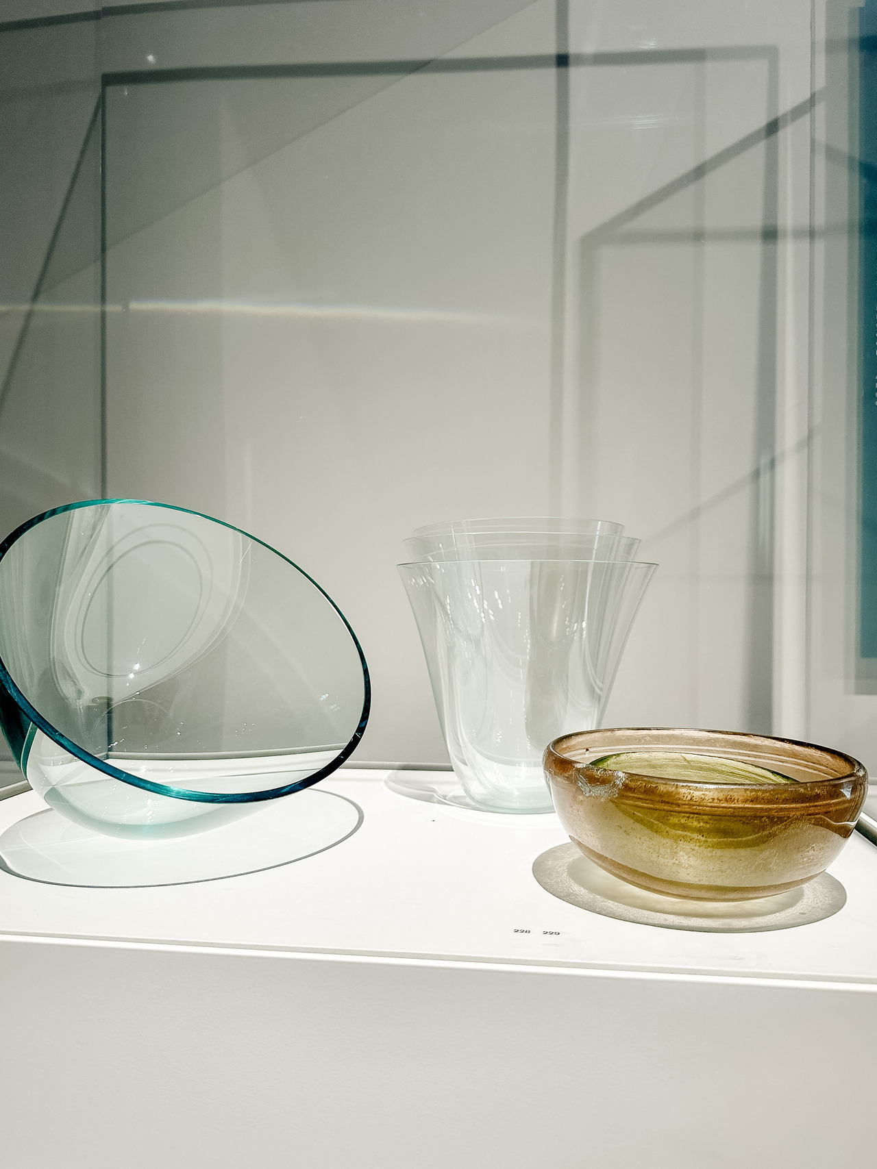 Contemporary glass bowls in clear, blue-green and amber tones displayed together in the Glass, Made in Antiquity exhibition.