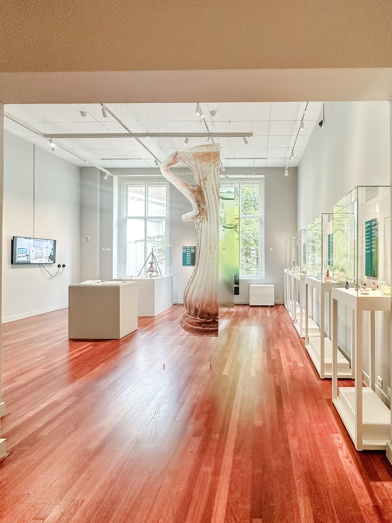 Interior of the Glass, Made in Antiquity exhibition at the Allard Pierson Museum in Amsterdam, featuring a large suspended image of an ancient glass vessel, wooden floors and illuminated display cases.