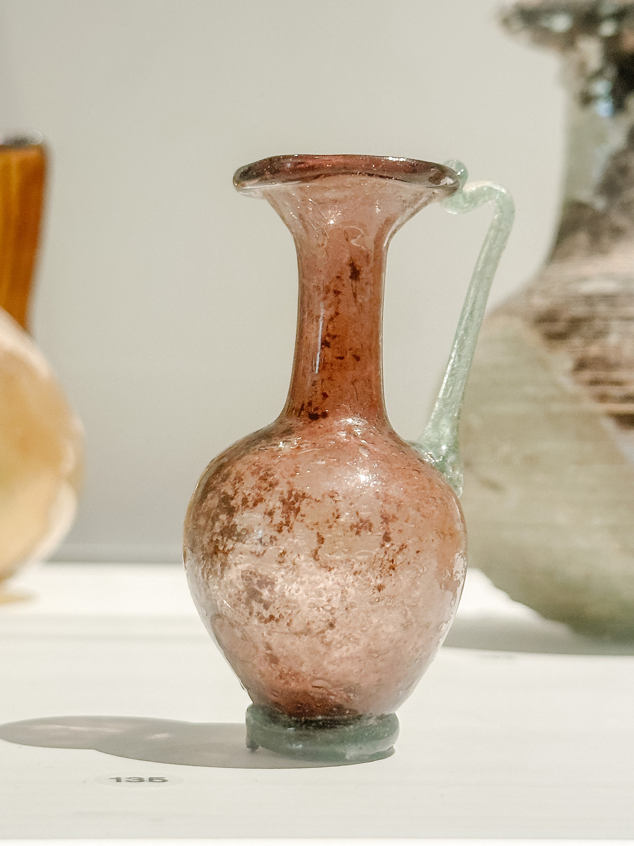 Close-up of an ancient pink glass jug with a rounded body, flared rim and pale green handle at the Allard Pierson Museum.