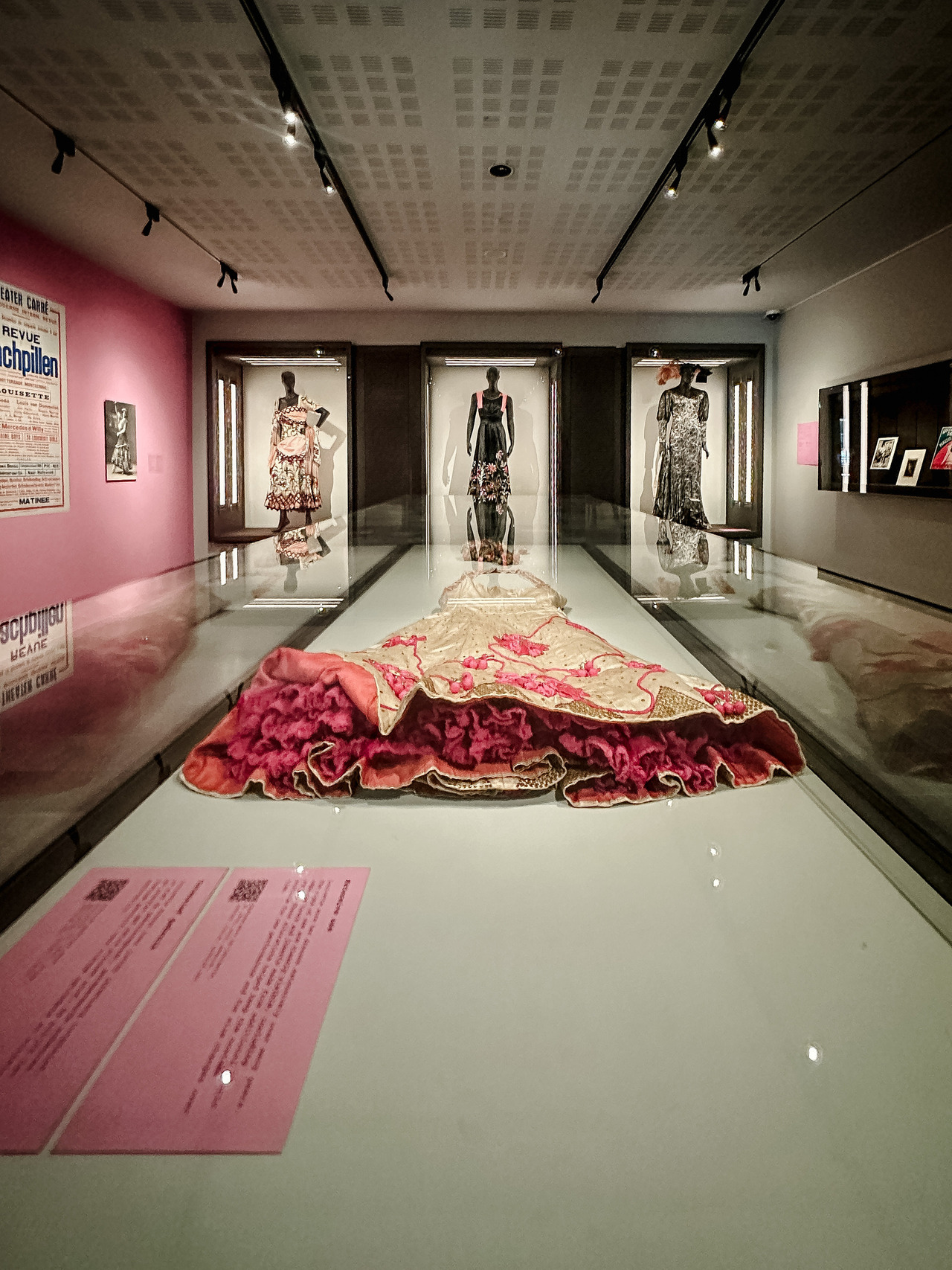 Elaborate theatrical costumes displayed at the Allard Pierson Museum, including a red embroidered garment in a glass case and three dresses on mannequins.
