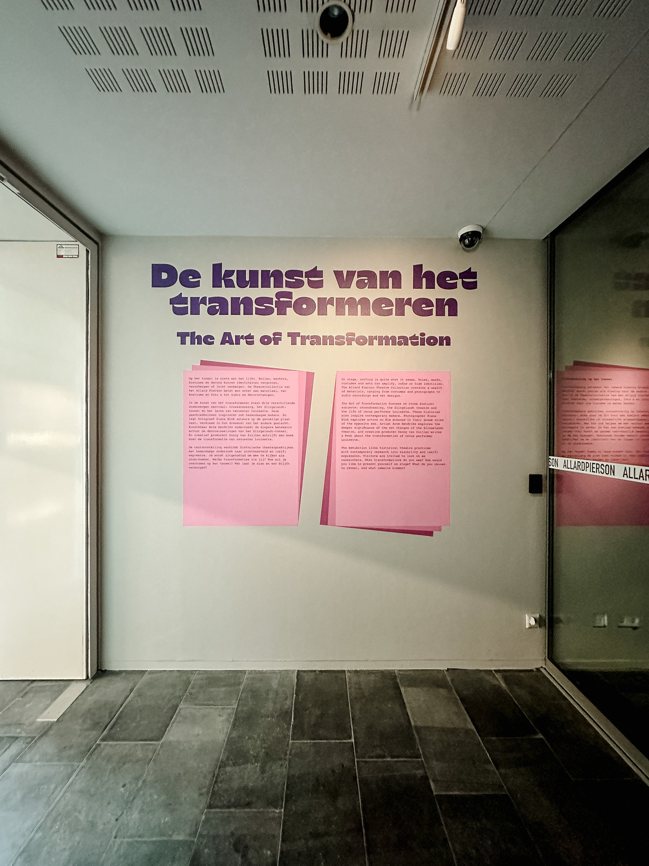 The Art of Transformation exhibition title in Dutch and English above two pink introductory information panels at the Allard Pierson Museum in Amsterdam.
