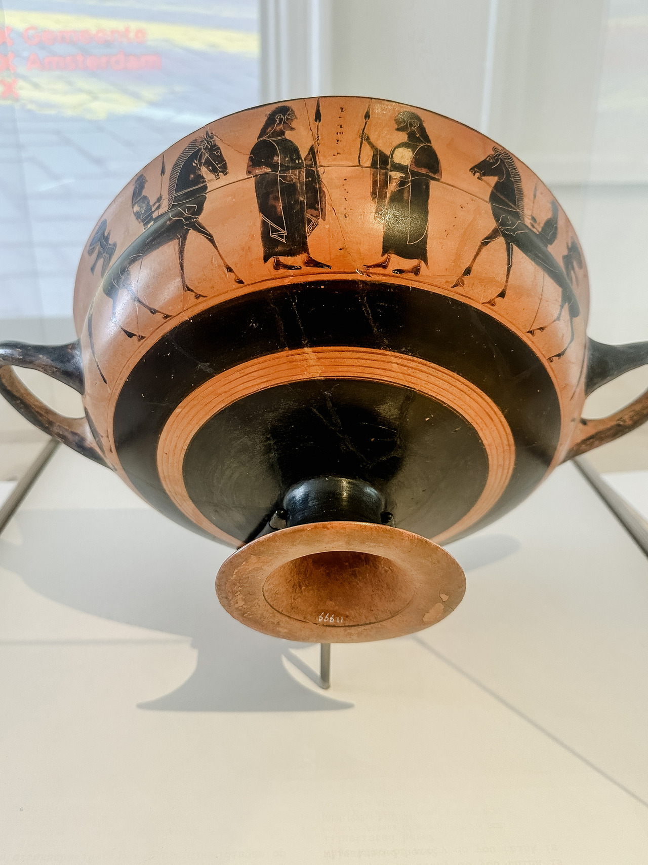 Underside of an ancient Greek black-figure drinking cup decorated with horses and standing figures, displayed at the Allard Pierson Museum.