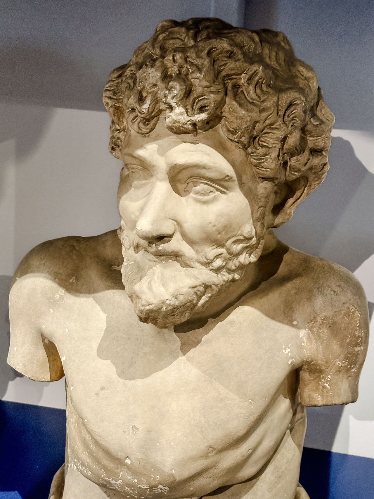 Close-up of a sculpted bust representing Aesop, with curly hair, a beard and a partially preserved torso, at the Allard Pierson Museum.