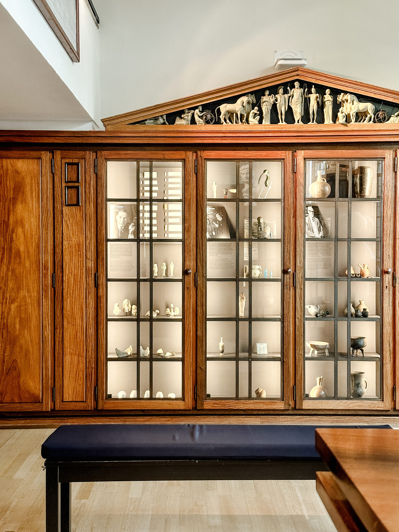 Historic wooden display cabinet with glass doors, archaeological objects and a decorative classical pediment at the Allard Pierson Museum.