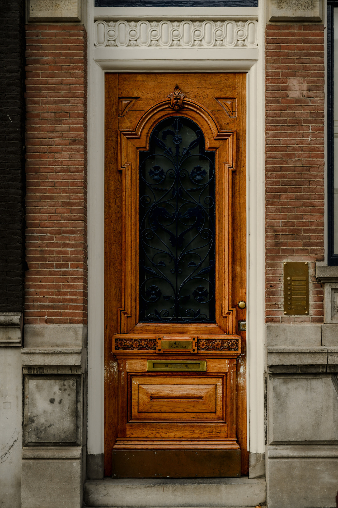 Ornately carved wooden entrance door with black decorative ironwork, framed by red brick and pale stone in Amsterdam.