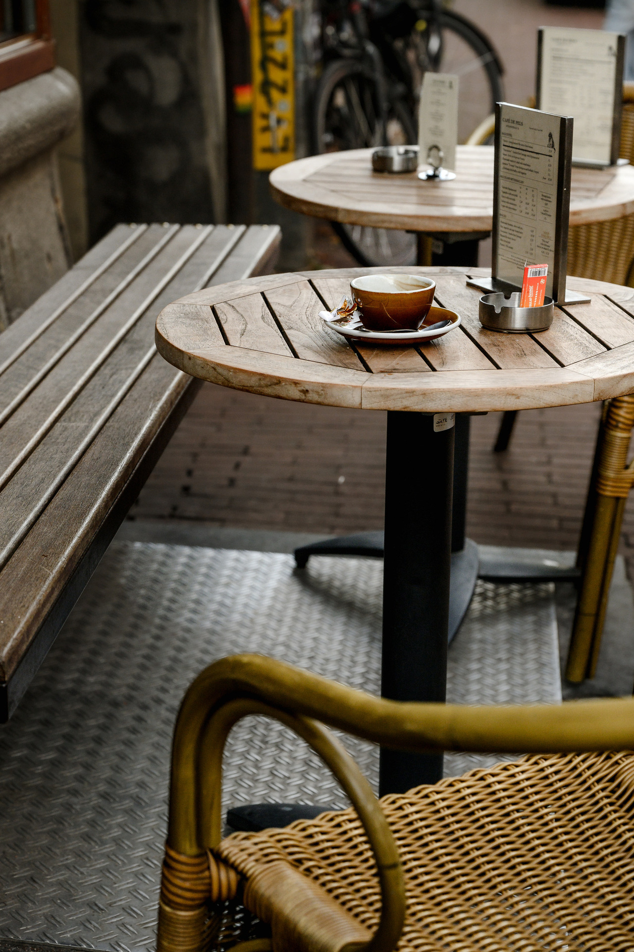 Small wooden café table with a used coffee cup, menu and wicker chair on an outdoor terrace in Amsterdam.
