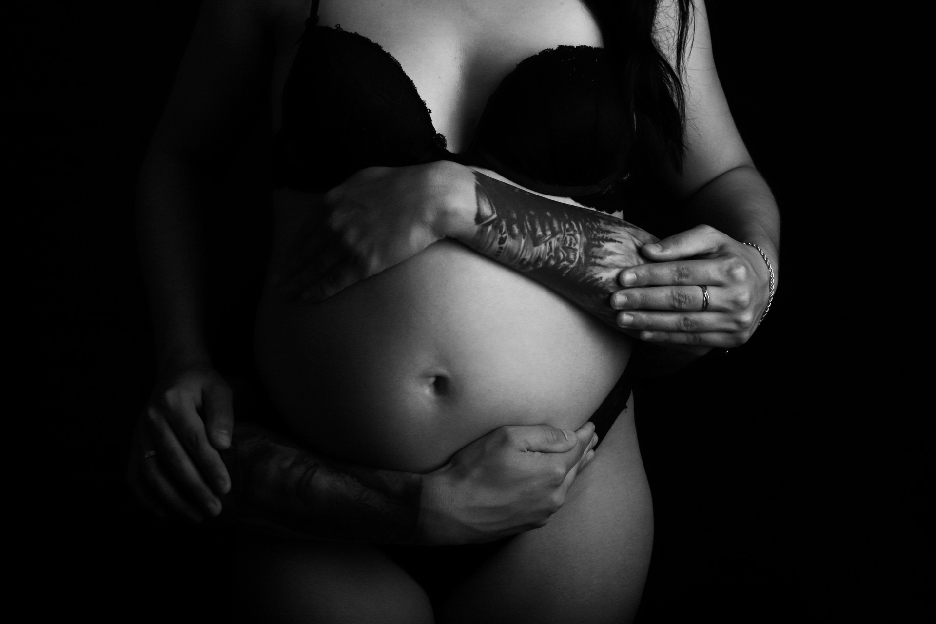 Fotografia Preto e branco de Gestante abraçando a barriga junto com o pai, com tatuagem no braço