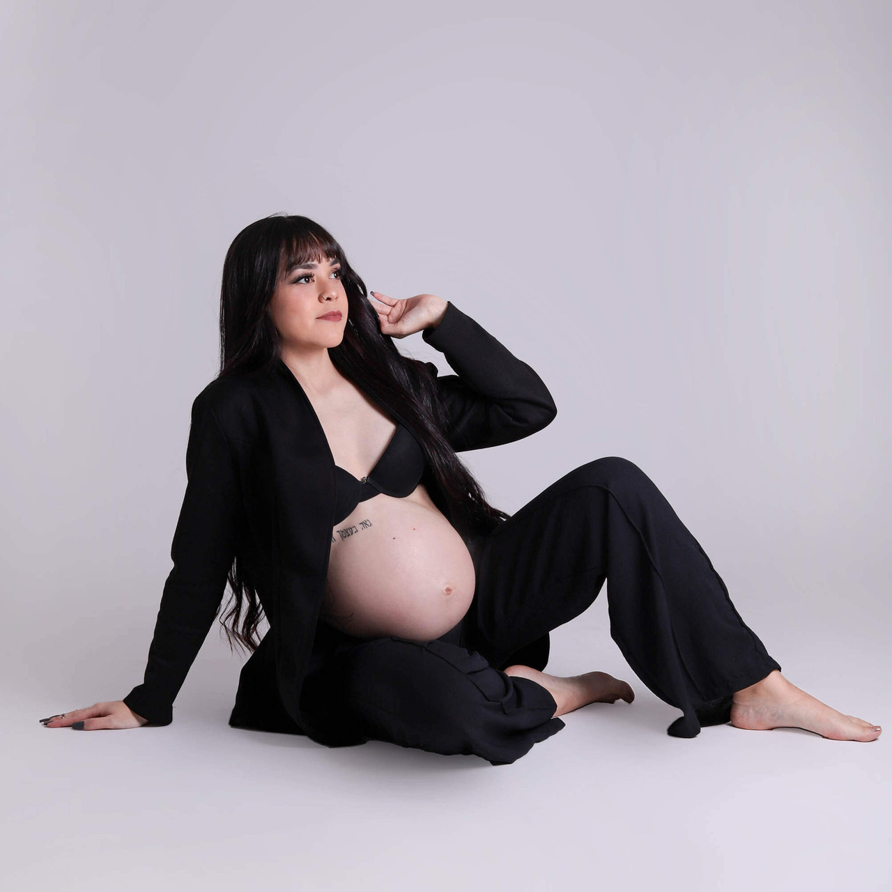 gestante sentada em fundo branco, com roupa preta olhando no horizonte, estúdio rossinis Fotografia de Gestante Suzano - São Paulo