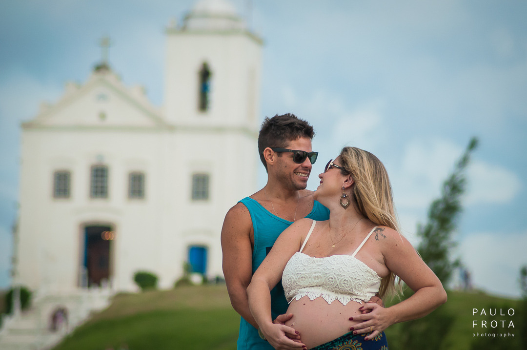 casal de gestante se olham. atrás deles a igreja de saquarema