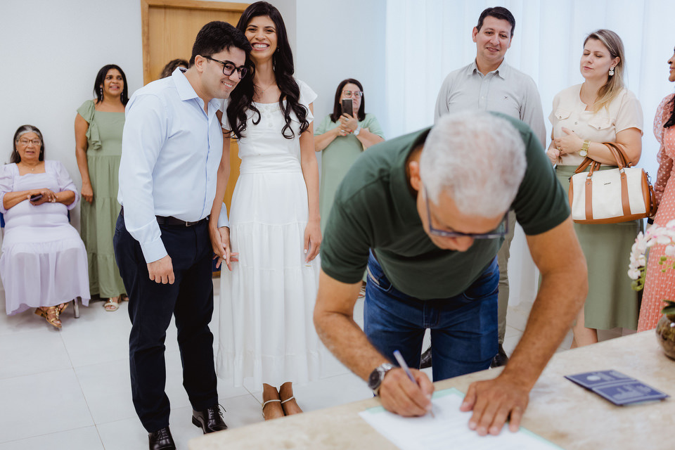Noivos abraçados sorrindo enquanto observam a assinatura do documento de casamento civil