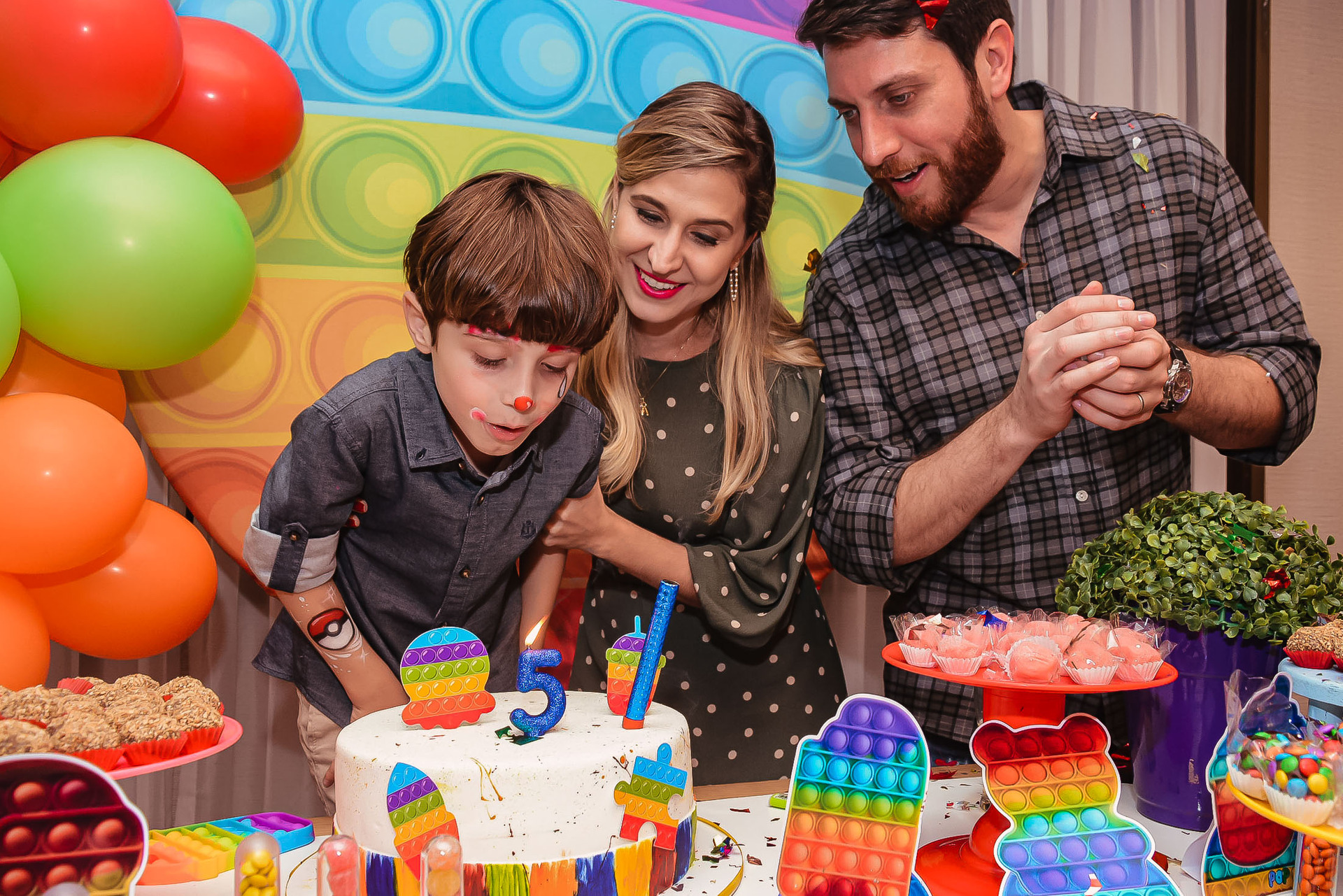 criança soprando vela de bolo de aniversário e seus pais observam e batem palmas