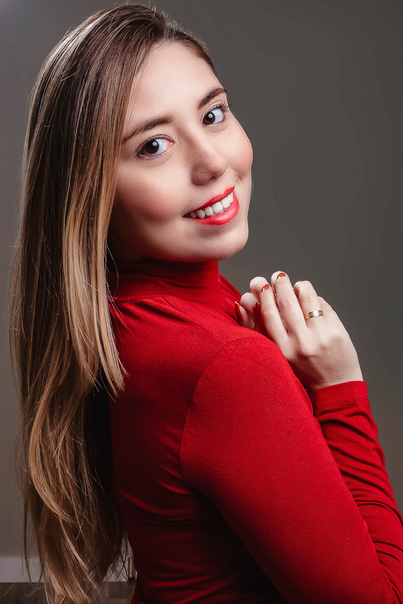 ensaio feminino em estúdio de modelo incluencer de niterói ela usa blusa vermelha de gola longa e sorri para a camera