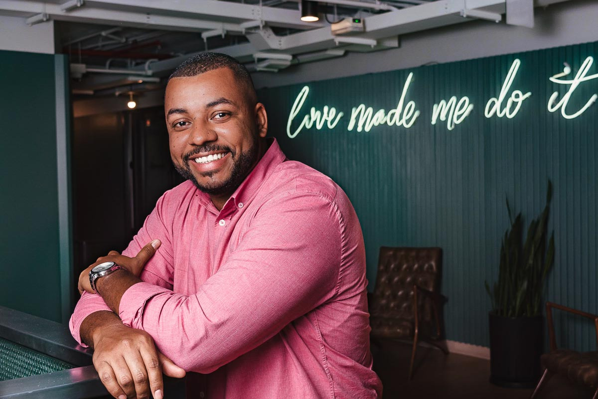 homem consultor financeiro apoiado em bacada sorri para a camera para sessão de fotos em coworking
