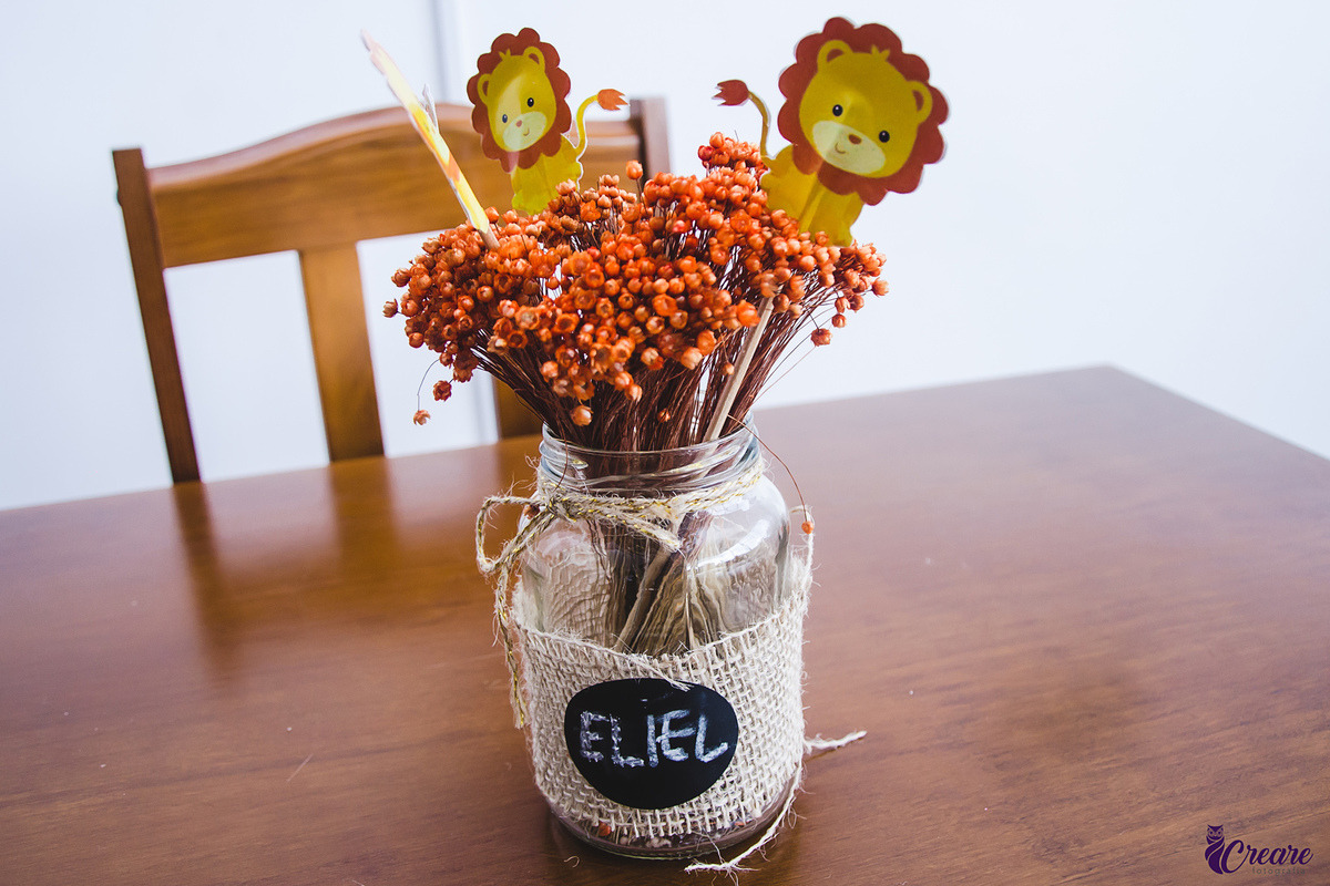 a imagem contem um pote de vidro com flores laranja e dois leãozinhos.