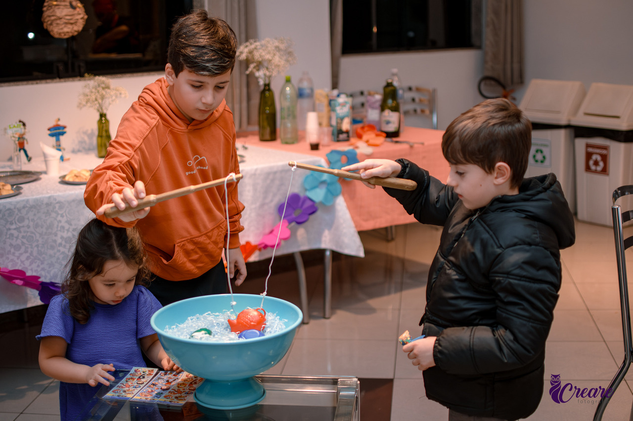 a Imagem contém 3 crianas brincando de pescar peixinhos de plástico em uma bacia.