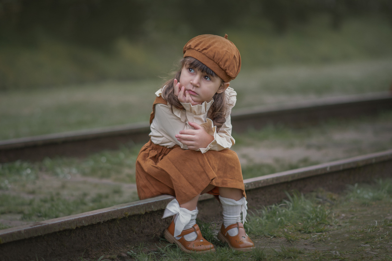 Uma menina, sentada em trilhos de trem e pensativa, durante seu ensaio fotográfico em Paranapiacaba.