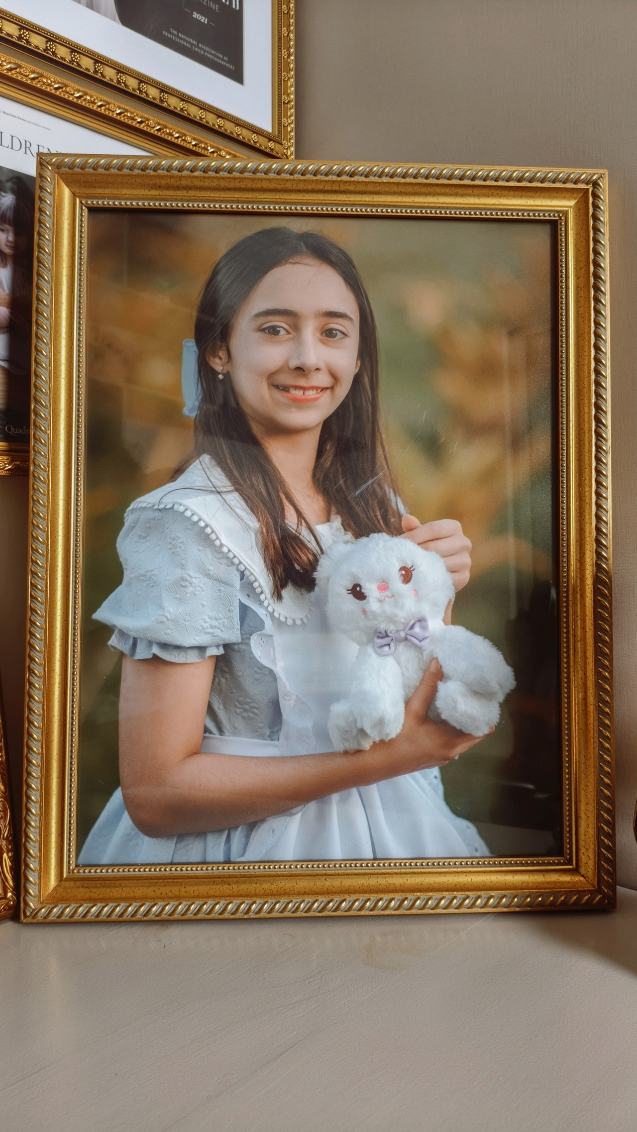 Quadro com a fotos de uma criança de 11 anos segurando um ursinho de pelúcia branco.