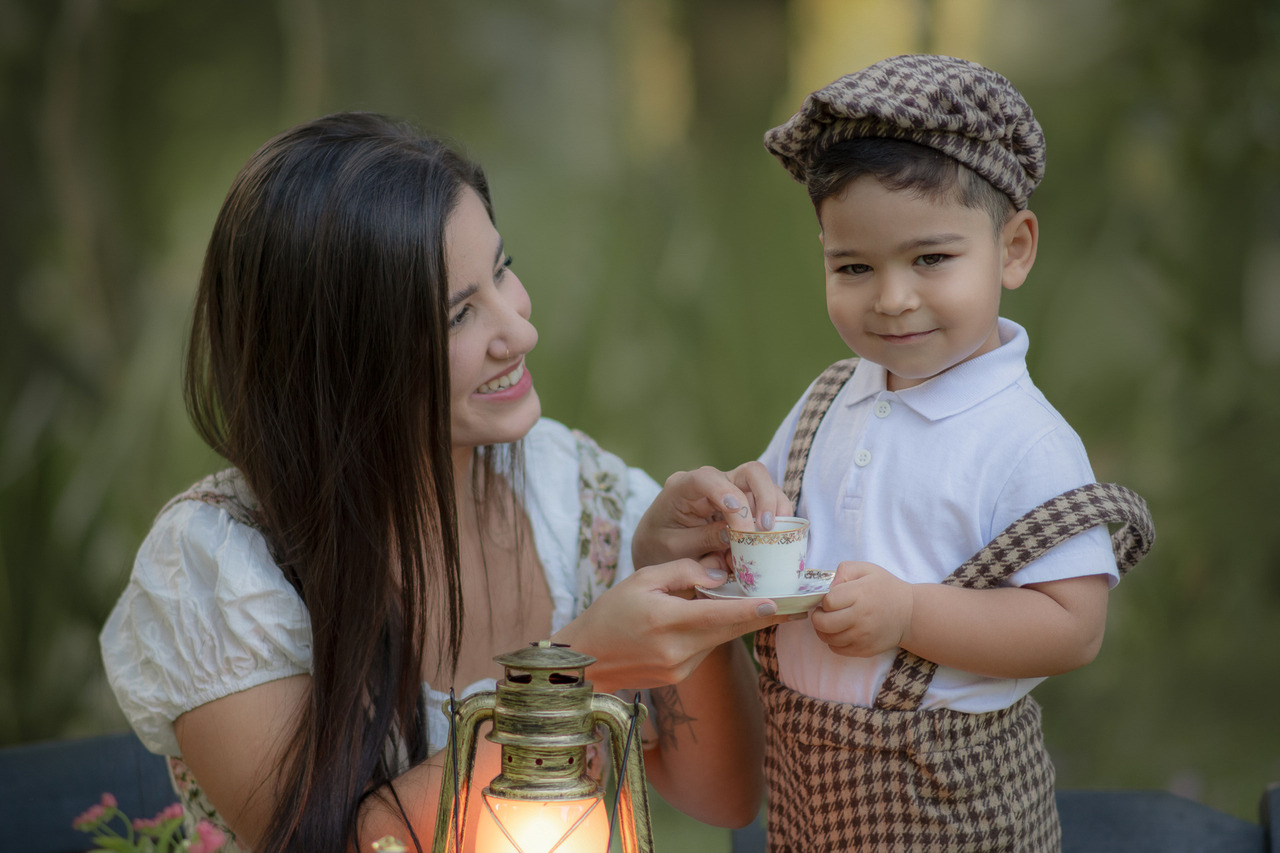 Uma mães brincando com seu filho de tomar chá, durante o ensaio fotográfico de dia das mães ao ar livre.