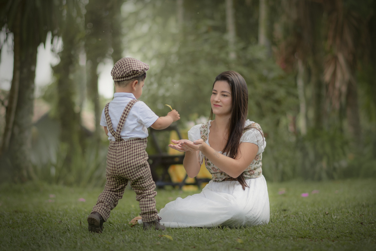Uma mulher brincando na grama com seu filho pequeno, durante o ensaio fotográfico de dia das mães.