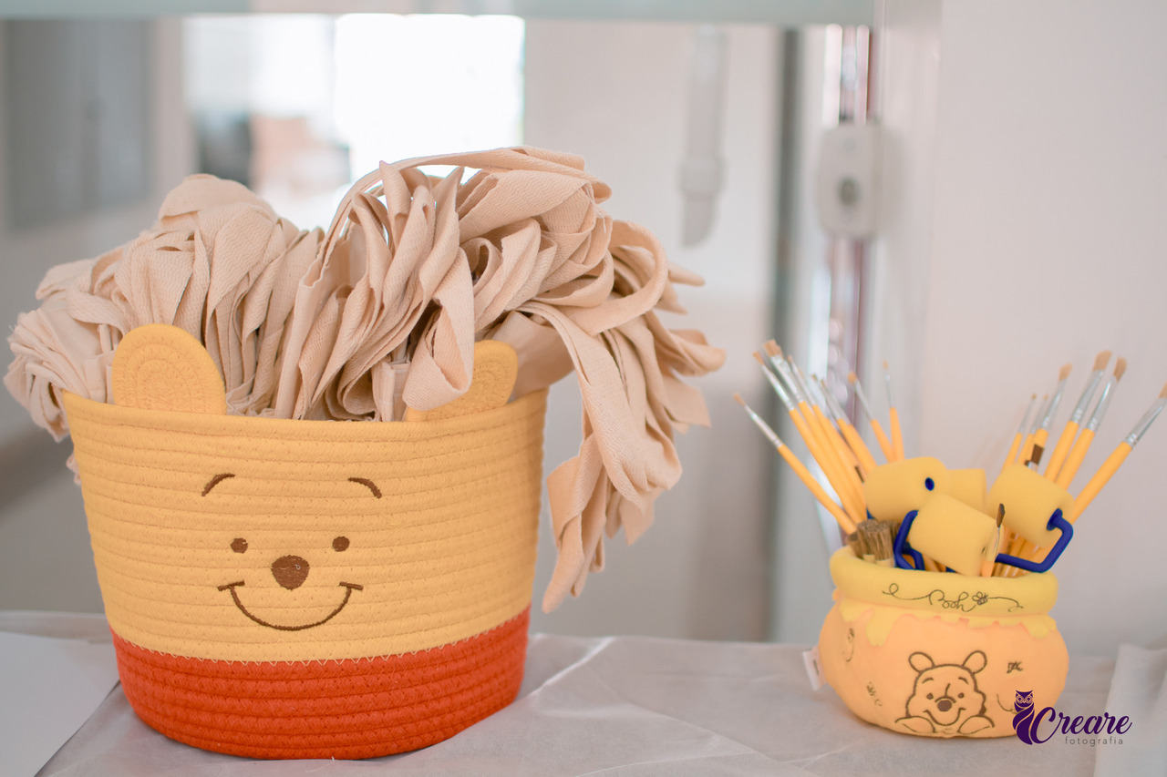 cesto com o rosto do Ursinho pooh, com ecobags para personalizar, ao lado um cesto com pincéis e rolo de tinta. 