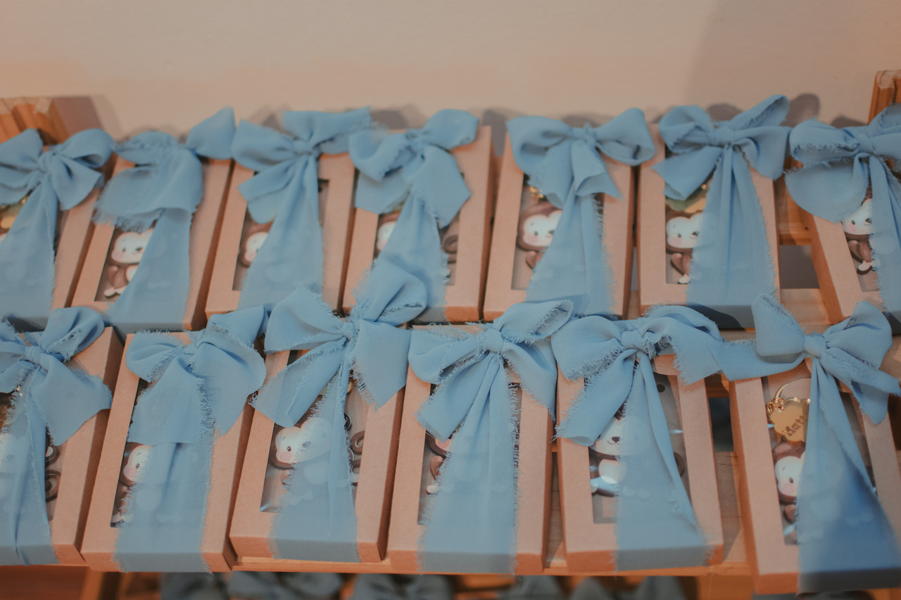 caixas com faixa azul, contendo um chaveiro de macaco, para lembrancinha de festa infantil.