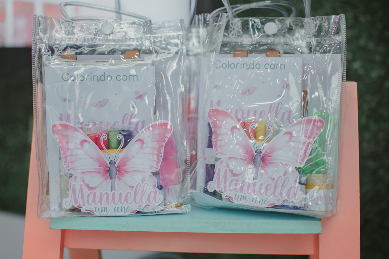 sacolas decoradas com uma borboleta rosa, contendo livros de colorir para lembrancinha de festa de 1 ano.