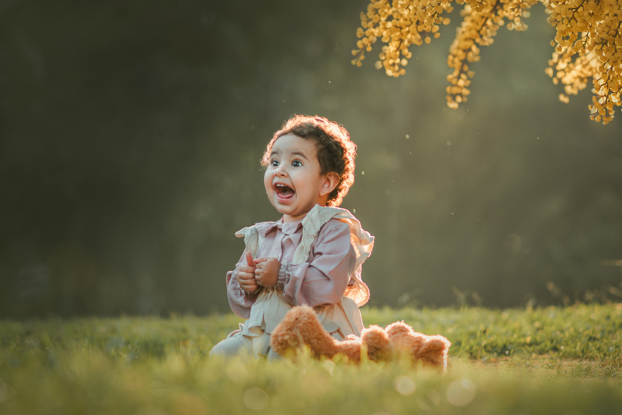 Uma menina, sorrindo e brincando na grama durante seu ensaio fotográfico de 1 ano.