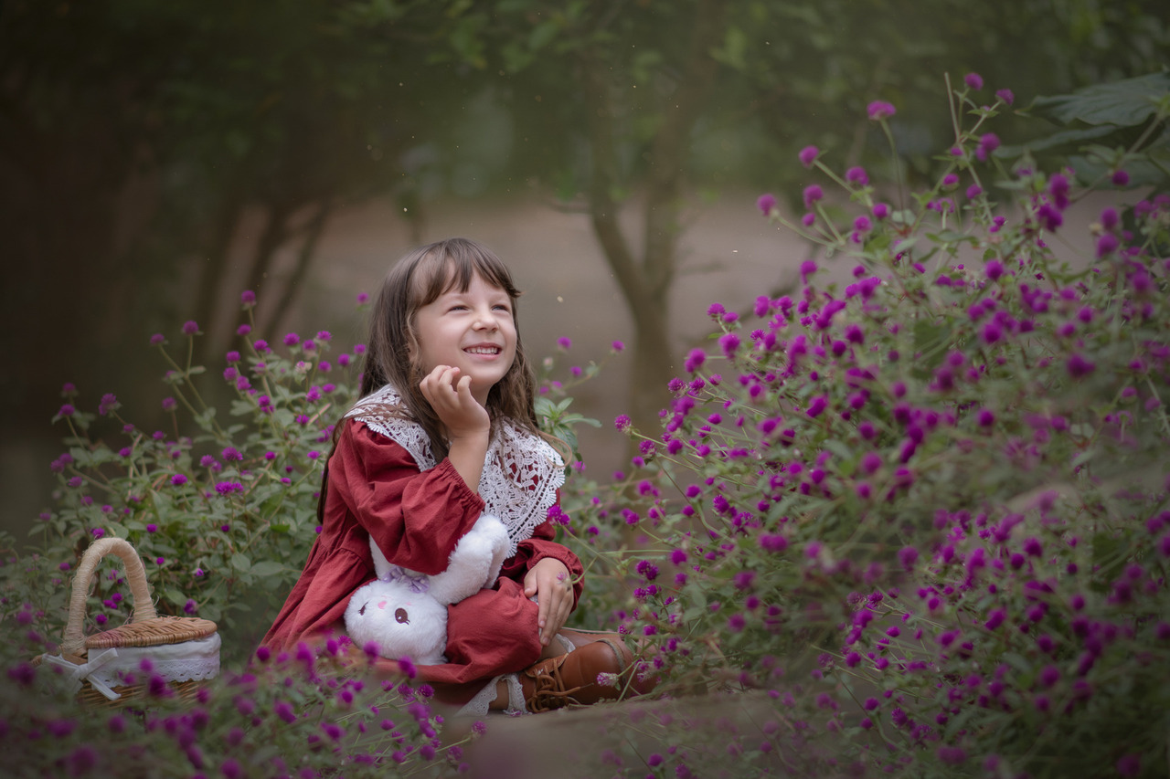 Uma menina usando vestido vermelho entre flores roxas, durante ensaio fotográfico em Santo André.