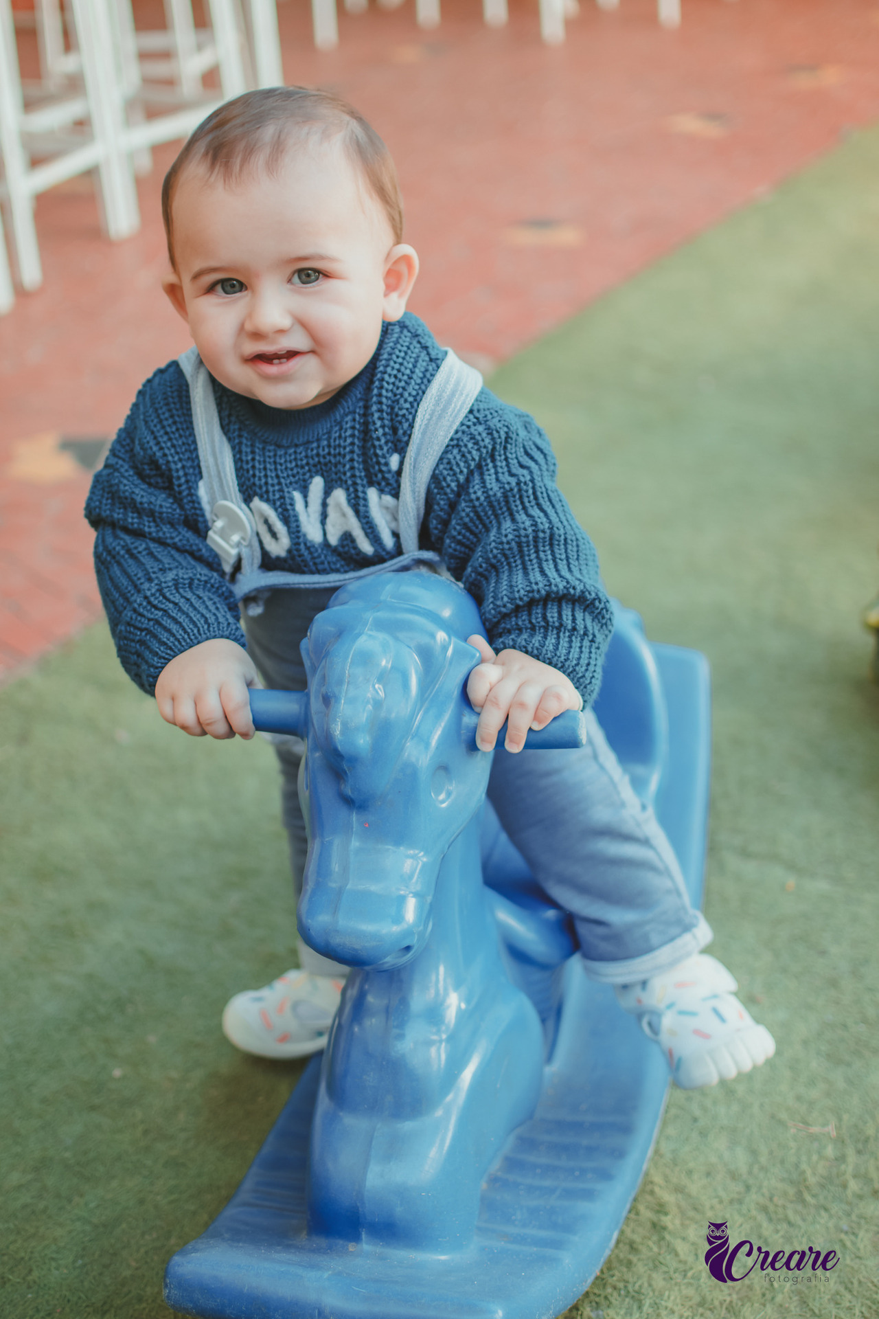 Um bebê brincando em um cavalinho azul de balanço.