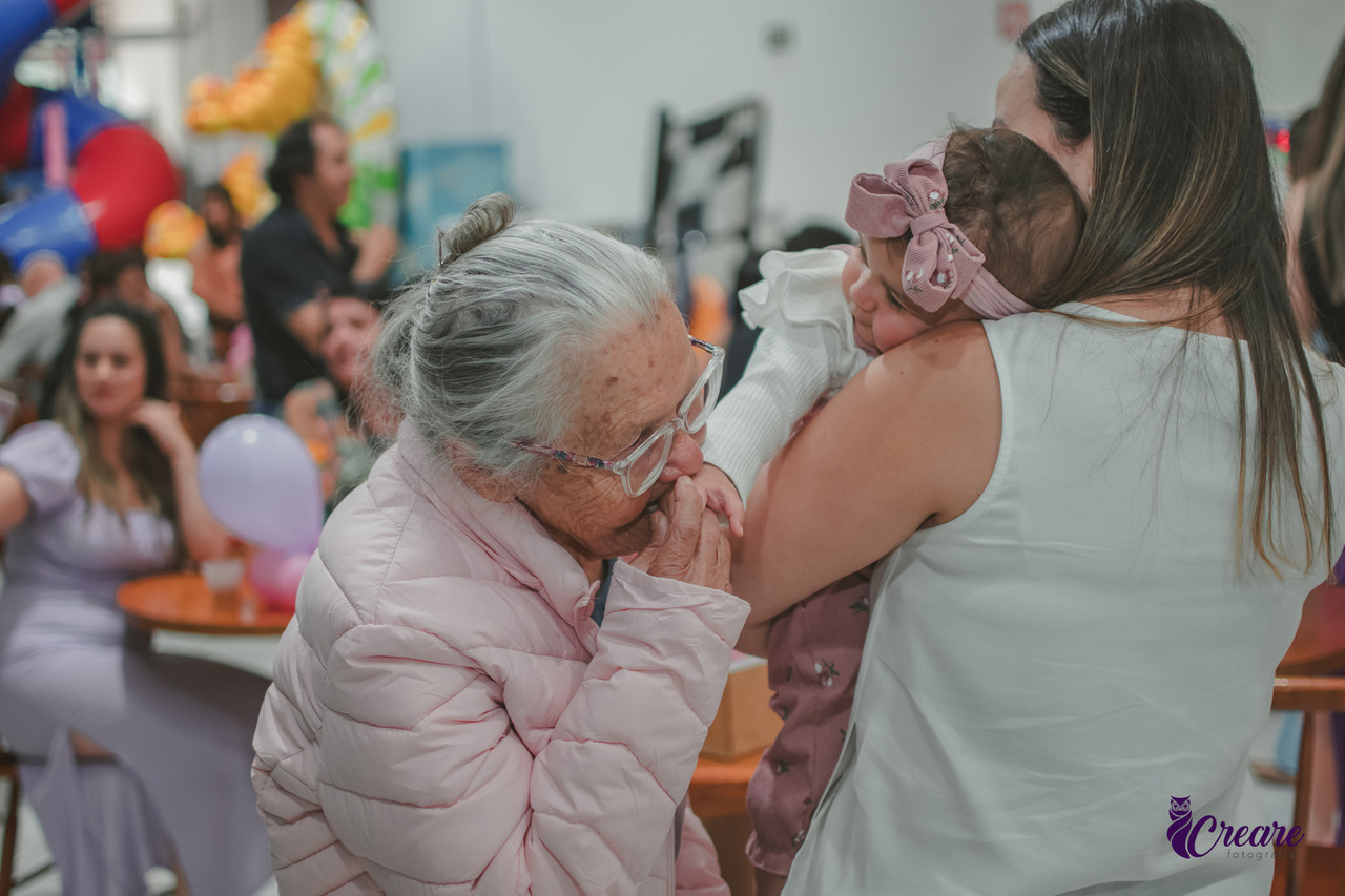 Uma senhora de idade beijando a mão de uma bebê, durante seu aniversário de 1 ano.
