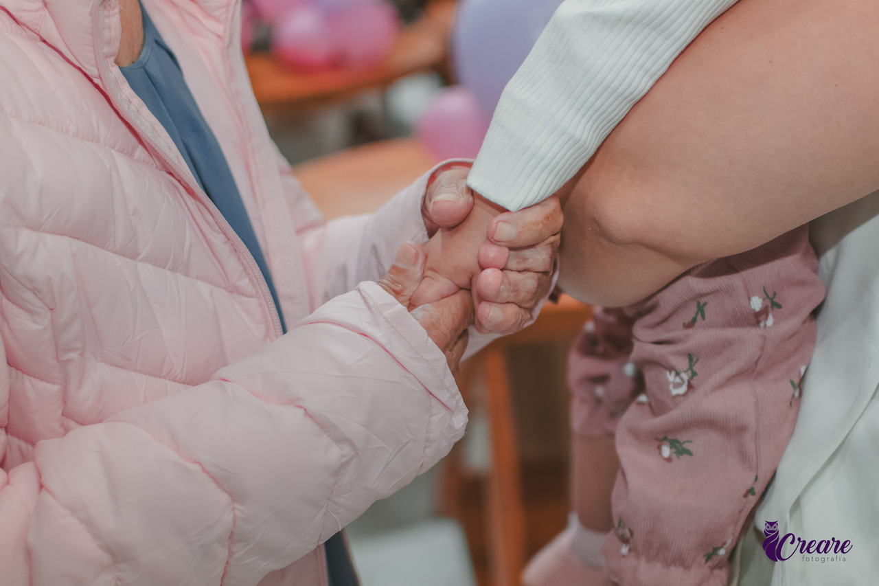 Detalhes da mão ded um bebê segurando a mão da sua avó, durante festa de aniversário infantil.
