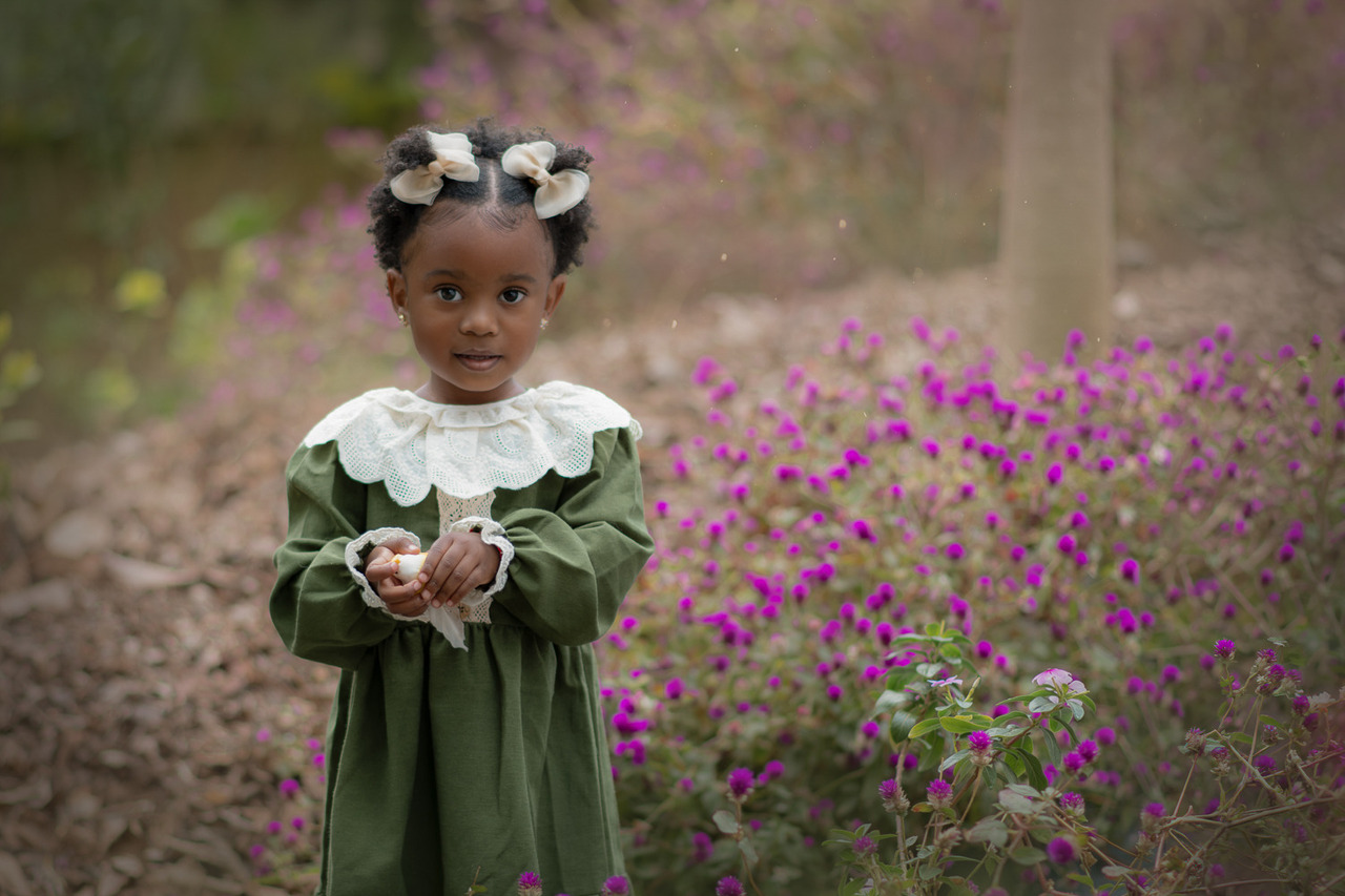Uma criança usando vestido verde entre flores roxas.