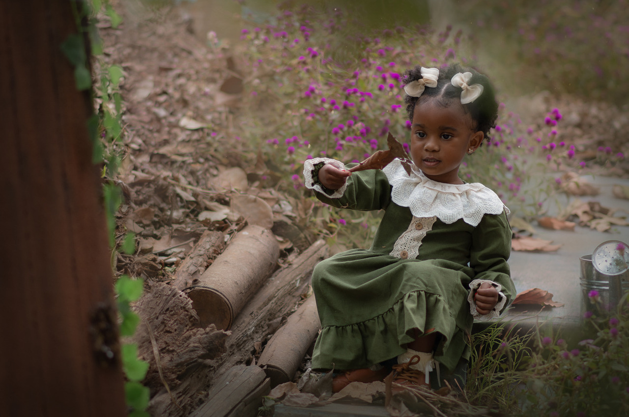 Uma menina usando vestido verde e segurando folhas secas, sentada na escada durante seu ensaio fotográfico externo.
