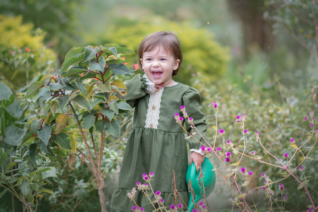 Uma menina, usando vestido verde, brincando com um regador de plantas, durante ensaio fotográfico em Santo André.