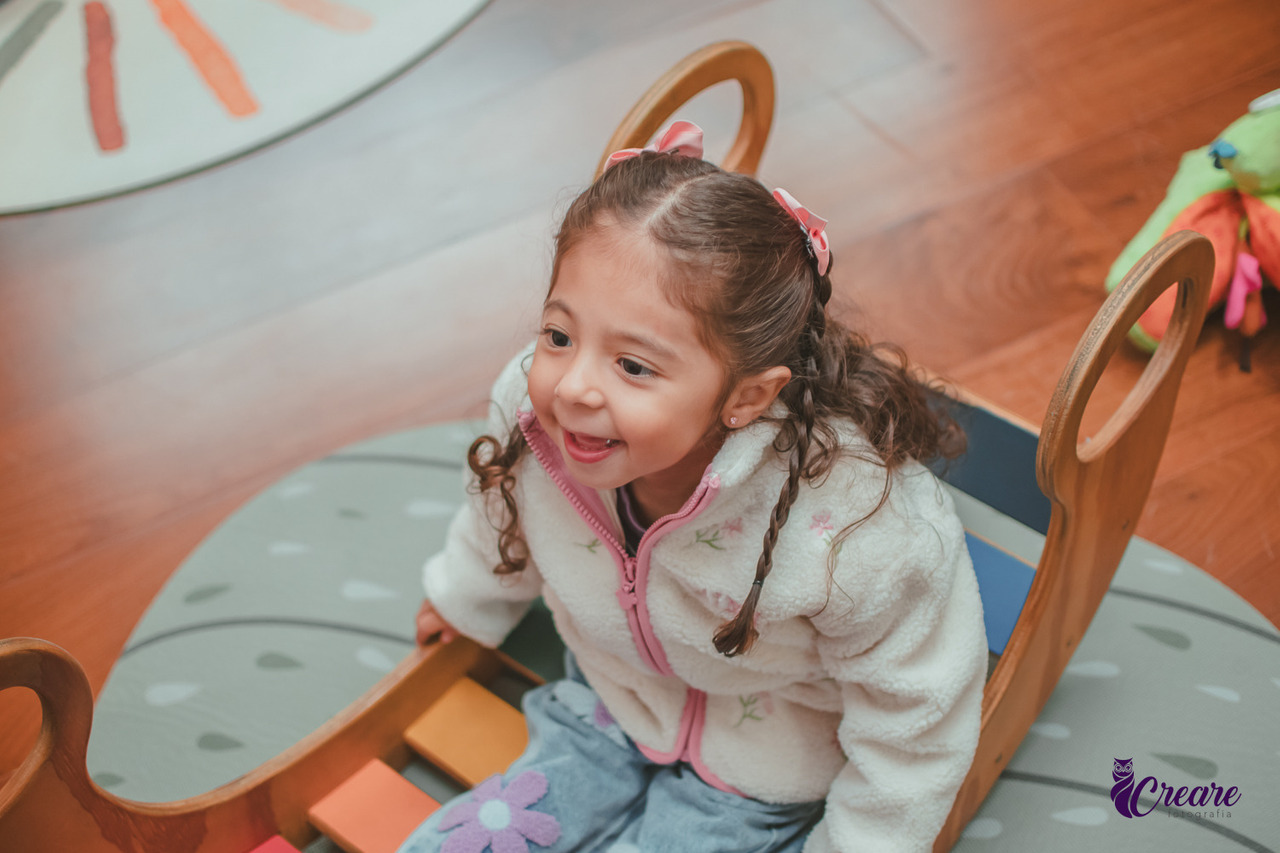 Uma menina sorrindo, enquanto brinca de se balançar, durante sua festa de aniversário de 3 anos.