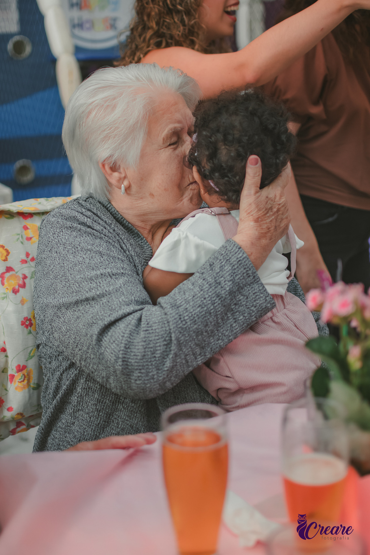 Uma avó abraçando sua neta de 1 ano, durante festa de aniversário.
