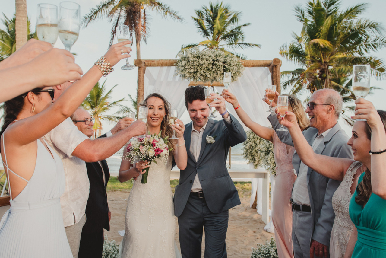 Noivos brindando seu destination wedding, frente ao mar e no por do sol com seus amigos e parentes