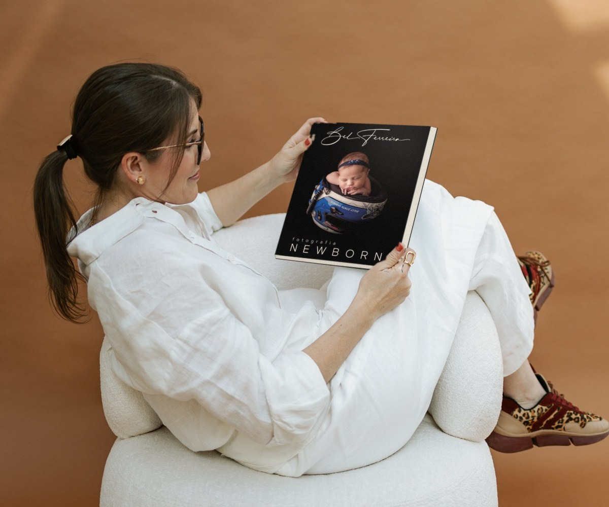 Bel Ferreira na poltrona do estúdio, lendo o livro Fotografia Newborn
