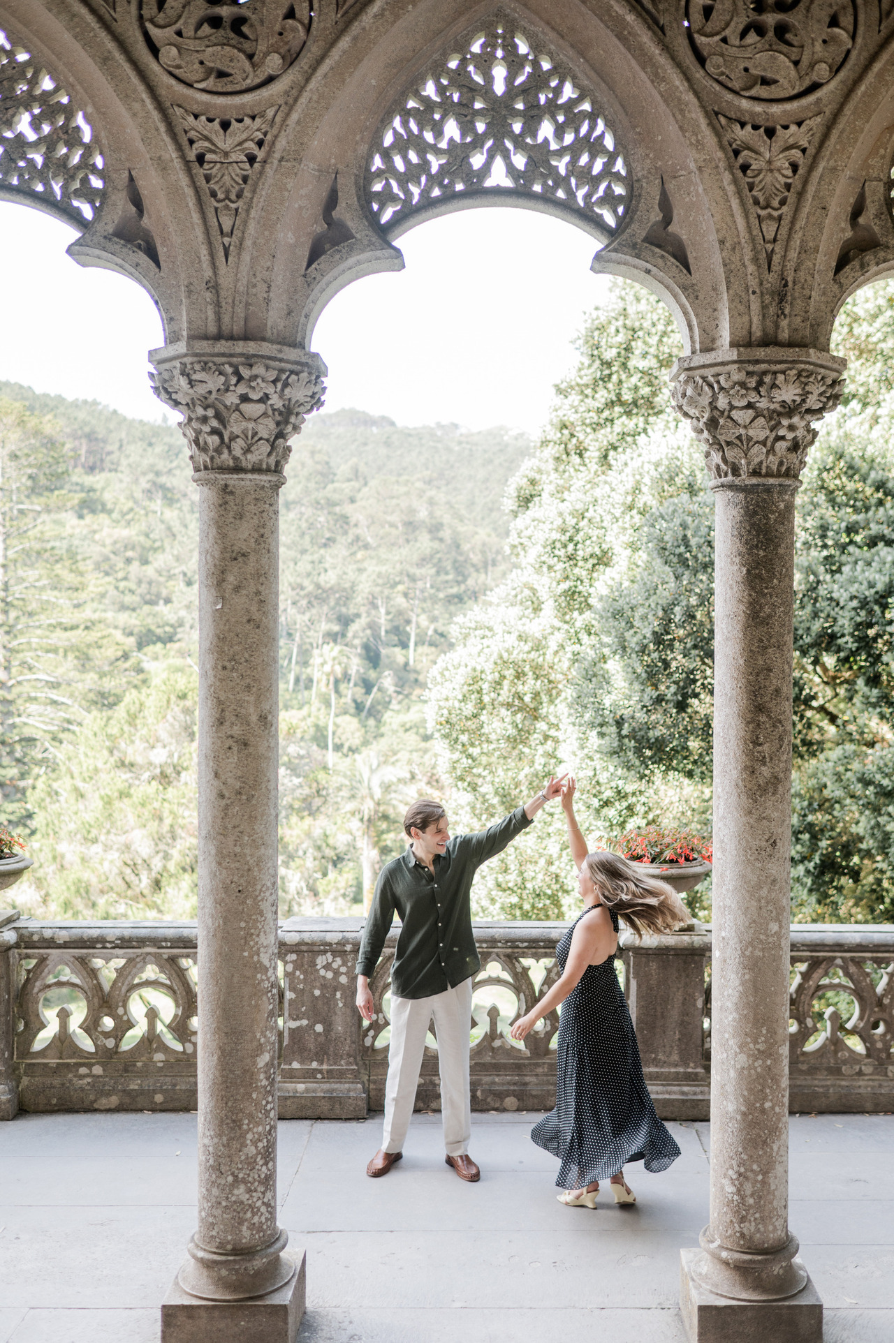 Zach spins Catherine under the stone arches of the terrace at Palácio de Monserrate, Sintra, engagement photography by Mariana Castanheira