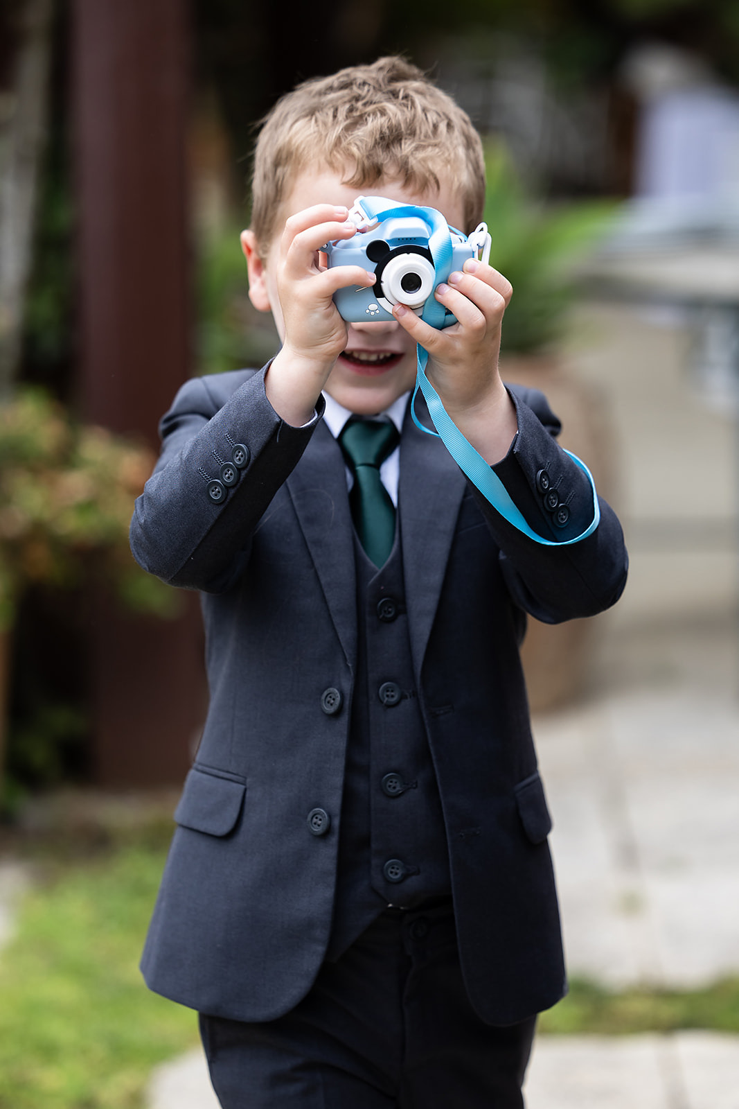 Criança vestida de fato a segurar uma máquina fotográfica de brincar apontada para a câmara. Foto por Filipe Santos, 2025.