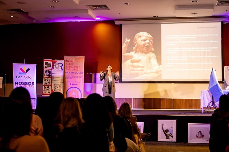Palestra da fotógrafa Juliany Gomes no congresso InFoco 2025, com simulação de parto em centro cirúrgico no palco, mostrando técnicas de fotografia de parto e fotografia documental.