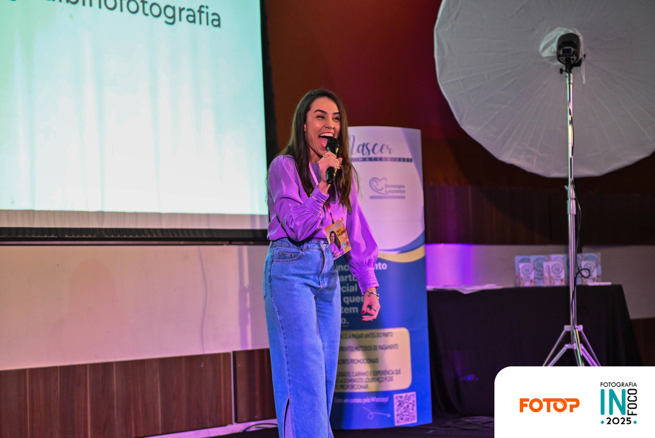 Palestra no congresso de fotografia InFoco 2025: palestrante apresenta conteúdo sobre fotografia no palco, com microfone em mãos, diante de fotógrafos participantes do evento.